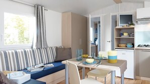 Une cuisine compacte avec un coin repas, comprenant un canapé à rayures, une petite table avec un saladier et des verres, et un meuble contenant de l’ustensile de cuisine.