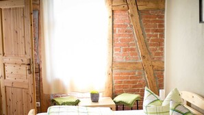 A bedroom with a wooden bed, a brick wall, a wooden ceiling, and a window with curtains. - Spring - Room 1 - Forsthaus Leiner Berg (Dessau-Roßlau)