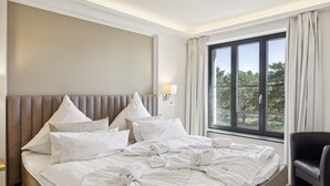 A hotel room with a large bed, a headboard, a nightstand, a lamp, and a window with curtains. - Amazing apartment in Binz with outdoor swimming pool (Prora/Rügen)