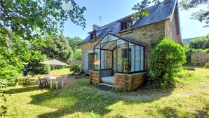 Ein Steinhaus mit Wintergarten, einer Terrasse mit Tisch und Stühlen sowie einem Garten.
