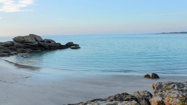 Ein Küstenstrand mit großen Felsen und ruhigem Wasser.