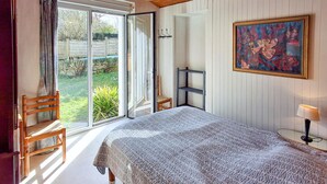Ein Schlafzimmer mit Bett, Sessel, einem kleinen Tisch, einem Bild und Blick auf den Garten durch das Fenster.