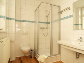 Kylpyhuone, jossa on lasiseinällä varustettu suihku, wc, pesuallas ja peili.