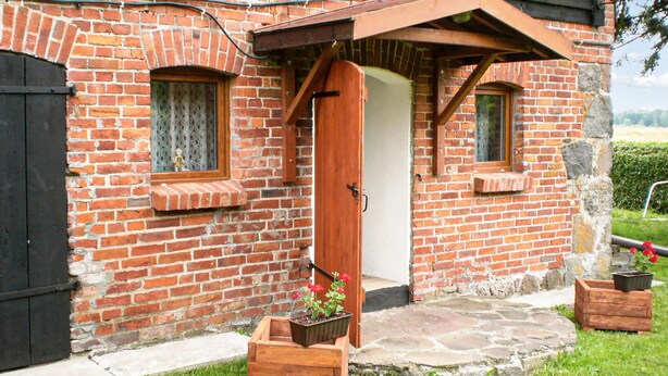 A rustic brick building with a wooden door, two windows with shutters, and a small garden area with potted plants. - Pet friendly apartment in Retowo 4 (Retowo 4)