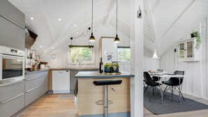 Eine moderne Küche mit Kochinsel, einem Essbereich inklusive Tisch und Stühlen sowie Blick ins Freie durch ein Fenster.