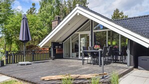 Ein modernes Haus mit einer Holzdiele, einer Glastür, die auf eine Terrasse führt, und Gartenmöbeln.