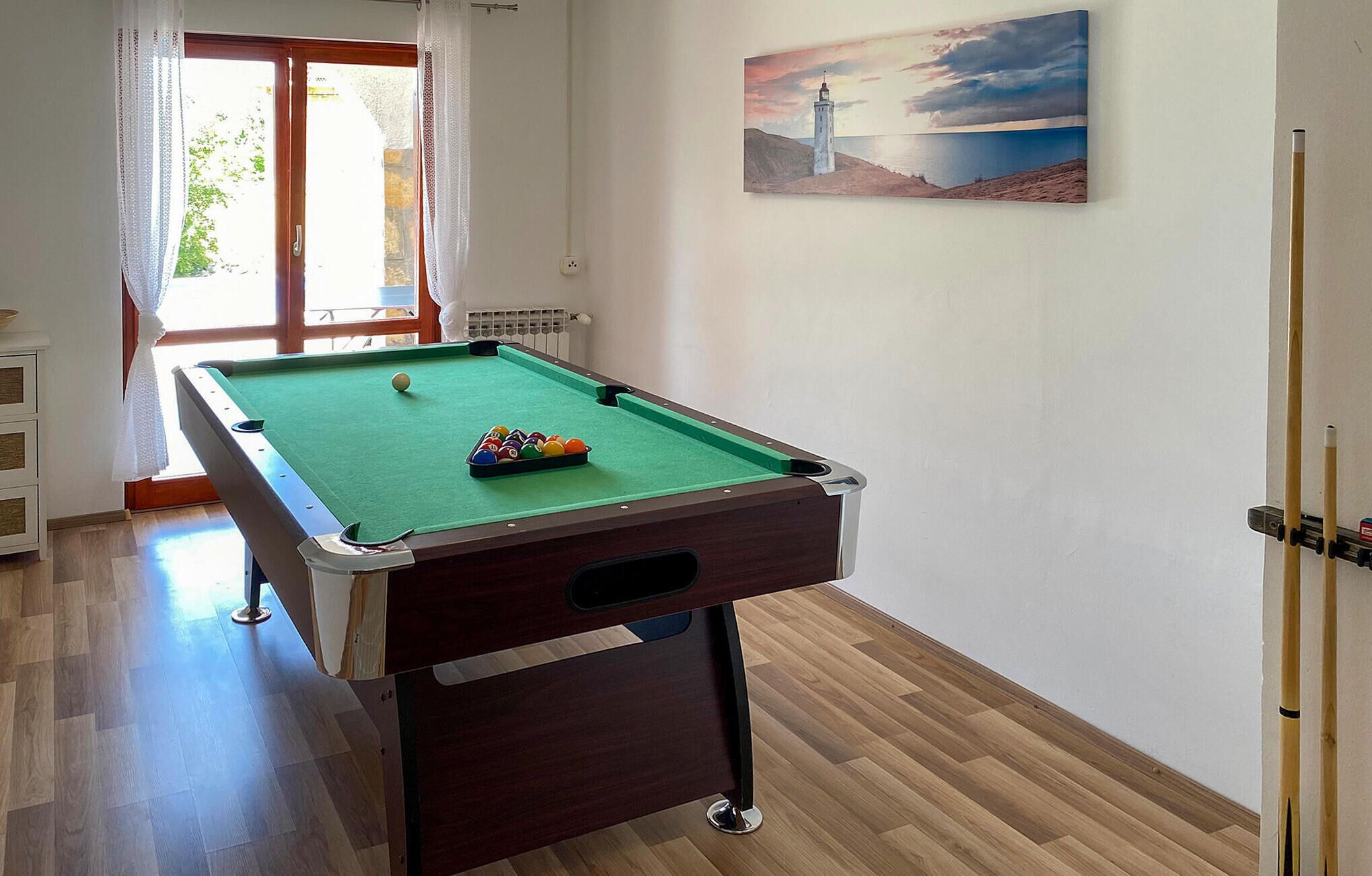 Una mesa de billar en una habitación con ventana, un cuadro en la pared y una puerta.