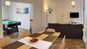 Un salon moderne comprenant une table de billard, une table à manger avec des sets de table, un canapé et un téléviseur.