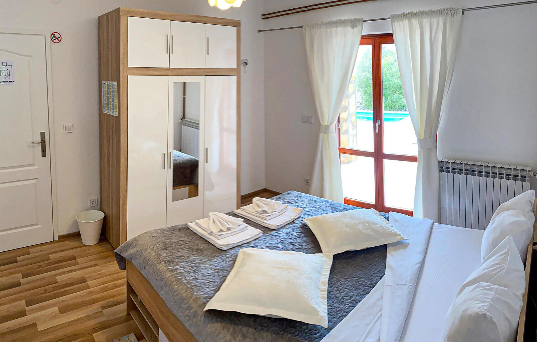 A bedroom with a bed, a wardrobe, a radiator, and a window with curtains.