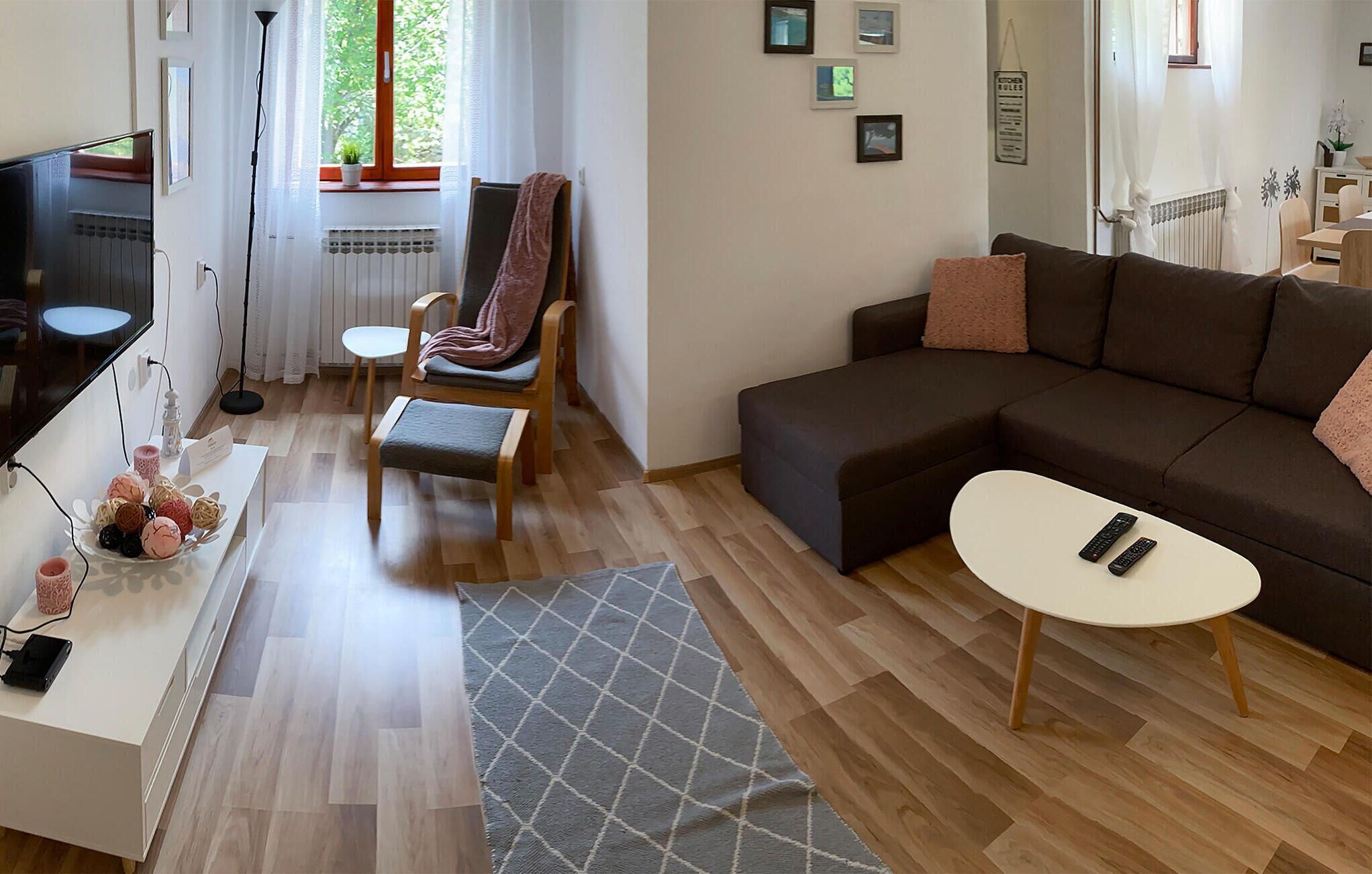 Ein Wohnzimmer mit Sofa, Sessel, einem kleinen Tisch, Fernseher und Heizkörper.