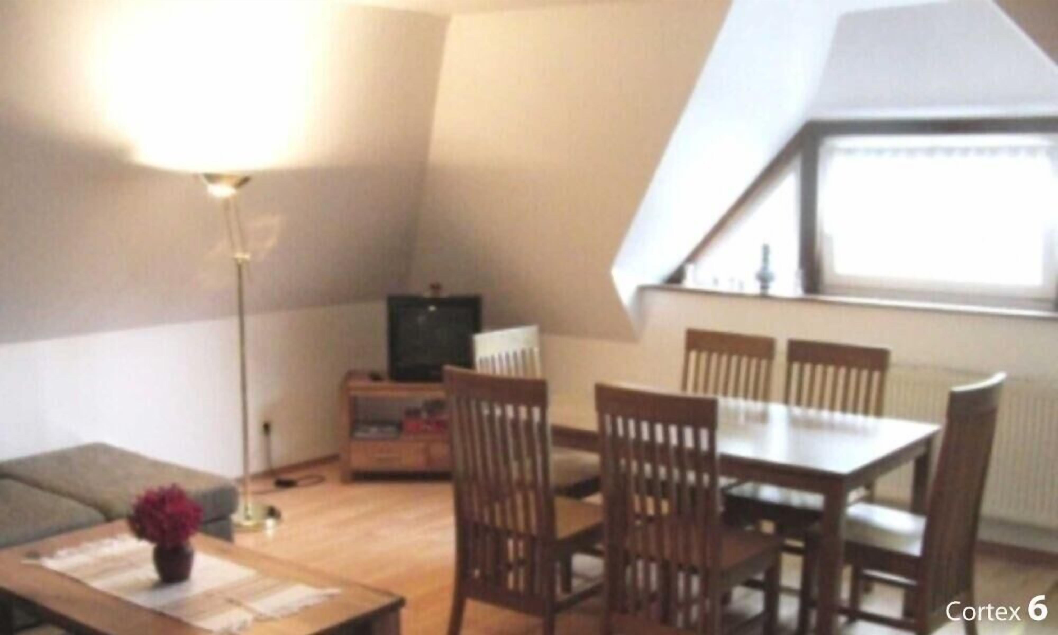 A small, cozy living room with a dining table and chairs, a TV, and a lamp.