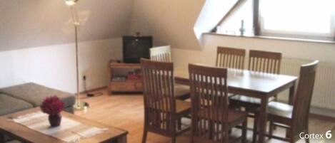 A small, cozy living room with a dining table and chairs, a TV, and a lamp.