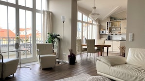 A modern living room with a sofa, chairs, a dining table, and a kitchen area. - (76) 3-room apartment with roof terrace lake view - Appartementhaus Atlantik (Kühlungsborn)