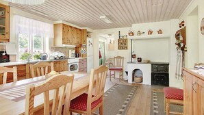 Una cocina acogedora con armarios de madera, una mesa de comedor y sillas. Hay una ventana que proporciona luz natural, y una chimenea con adornos encima.