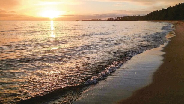 Una playa con un atardecer sobre el agua.