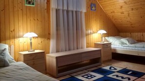 A cozy attic bedroom with wooden walls, a bed, a nightstand, a desk, and a window with curtains.