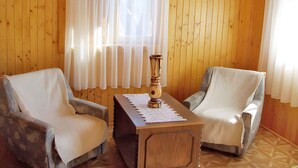 A room with wooden panel walls, two armchairs, a small wooden table with a globe and a vase, and sheer curtains.