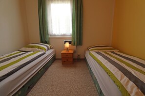A small, cozy room with two single beds, a nightstand with a lamp, and a window with curtains.