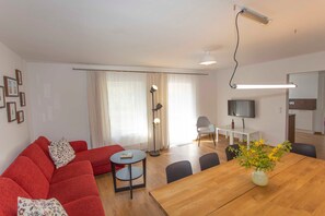 A modern living room with a red sofa, a wooden dining table, and a TV in the background. - House 8 - Rügen-Fewo 280/3 (Dreschvitz)