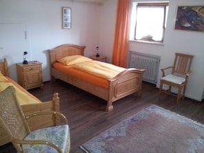 A bedroom with a wooden bed, a nightstand, a chair, a window with curtains, and a radiator.