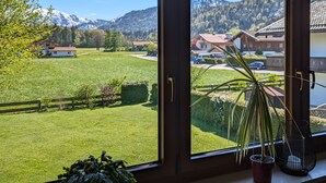 Une pièce dotée de grandes fenêtres donnant sur un champ verdoyant, une chaîne de montagnes et un quartier résidentiel.