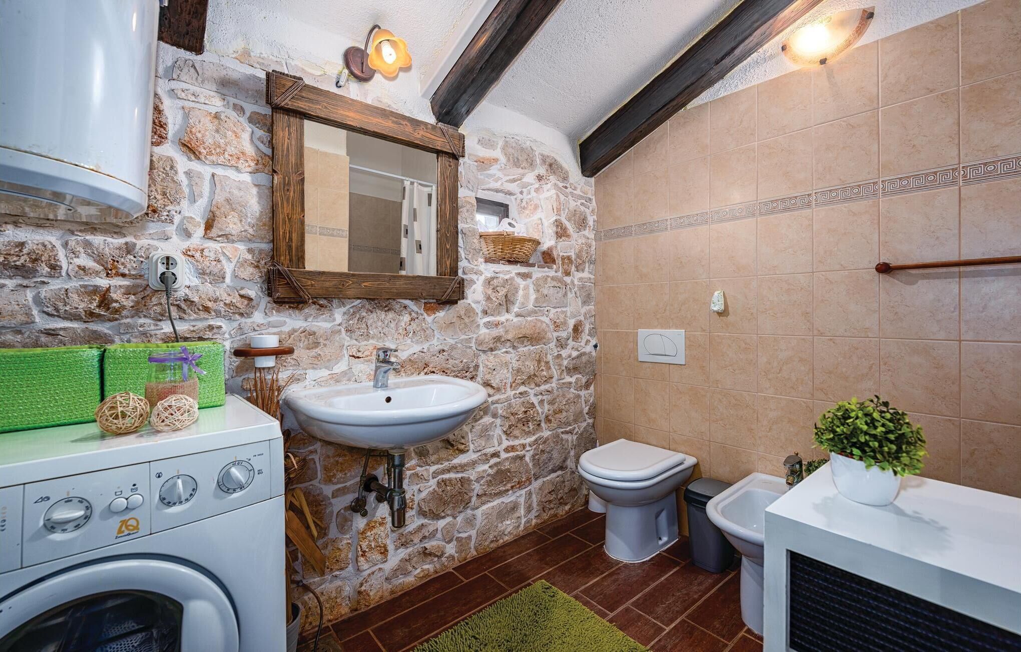 A bathroom with a stone wall, a wooden beam ceiling, a sink, a toilet, and a washing machine.