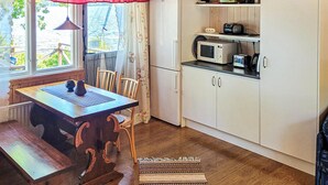 Una pequeña cocina con microondas, cafetera y refrigerador. Hay una mesa de madera con sillas y una ventana con vistas al agua.