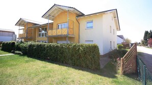 Ein zweistöckiges Wohnhaus mit Balkon und einem eingezäunten Garten, bewölkter Himmel.