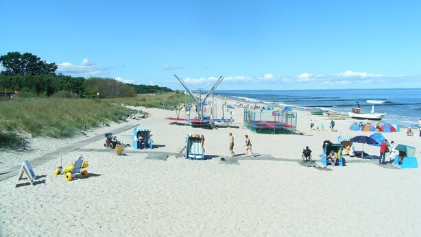 Ein Strand mit Sandweg, Liegestühlen, Sonnenschirmen und einem Rettungsschwimmerstand.