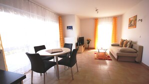 Ein Wohnzimmer mit einer Couch, einem Esstisch mit Stühlen, einem Fernseher und einer Heizung.