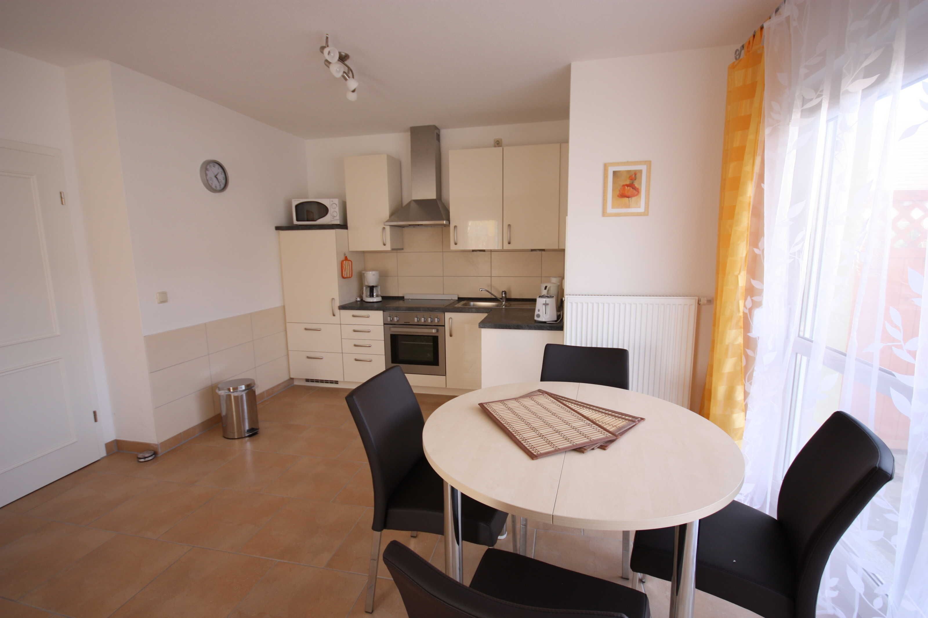 A compact kitchen with a dining area, a clock, and a radiator.
