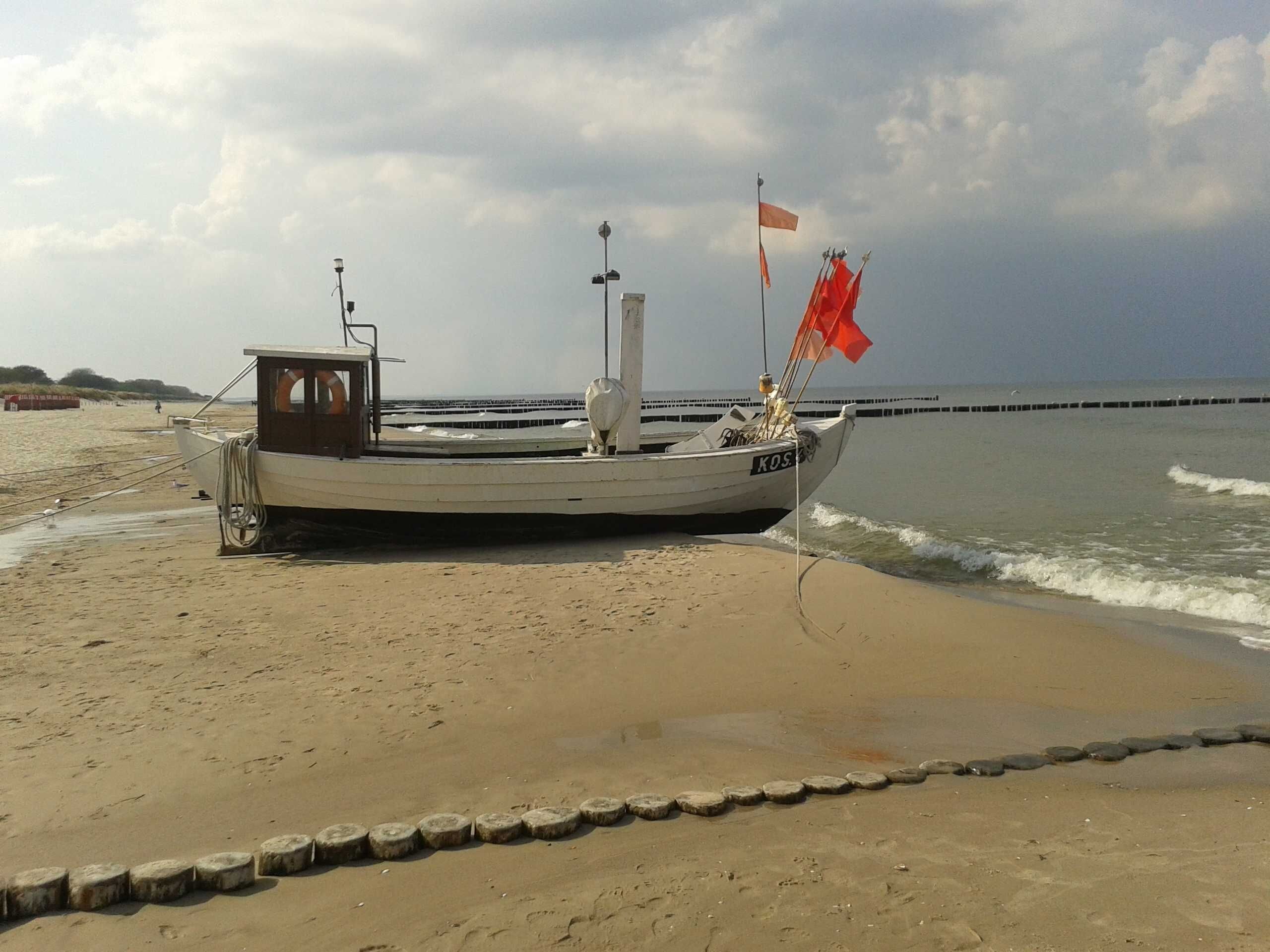 A boat on a sandy beach with a rocky breakwater in the background.