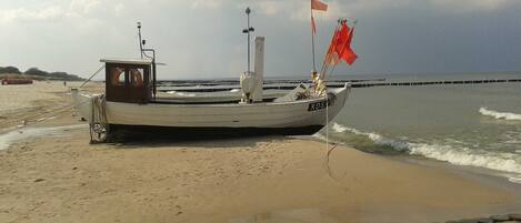 Ein Boot an einem sandigen Strand, im Hintergrund ein Felssteg.