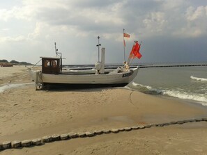 A boat on a sandy beach with a rocky breakwater in the background.