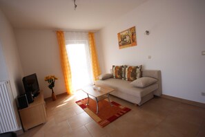 Una sala de estar con un sofá, una mesa de centro, un televisor sobre un mueble, un jarrón con flores y un cuadro en la pared.