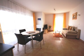Una sala de estar con sofá, mesa de comedor con sillas, televisión y radiador.