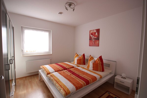 A bedroom with a bed, a nightstand, a window, and a radiator.
