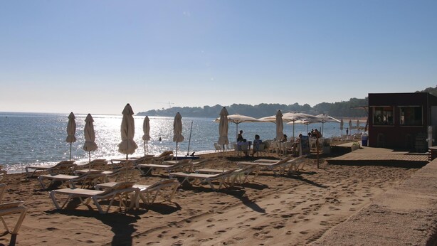 Ein Strand mit Liegestühlen und Sonnenschirmen, einem Rettungsturm und freiem Blick auf das Meer.