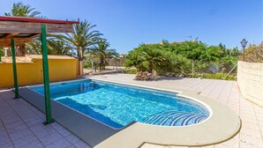 Ein rechteckiger Swimmingpool mit gefliestem Rand, umgeben von einer gefliesten Liegefläche und einer niedrigen Mauer.