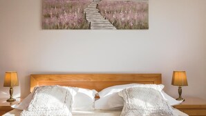 Een slaapkamer met een houten hoofdbord, twee bedlampen en een schilderij van een veld en pad boven het bed.