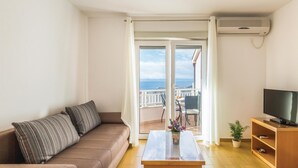 Een woonkamer met een bank, een salontafel, een televisie en een balkon met uitzicht op zee.