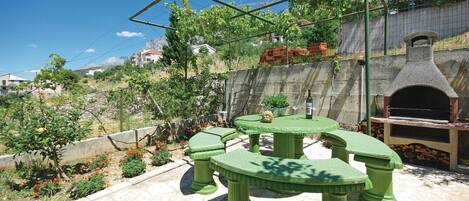 Eine Terrasse mit einem grünen Tisch und Stühlen, einer Steinmauer und einem Backofen aus Ziegeln.