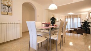 A dining area with a glass table, white chairs, a chandelier, and a dining table set with a bottle and glasses. - 2 bedroom nice apartment in Pula (Pula)
