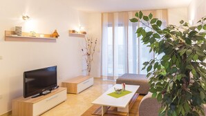 A modern living room with a flat-screen TV, wooden furniture, a coffee table, and a large plant. - 2 bedroom nice apartment in Pula (Pula)