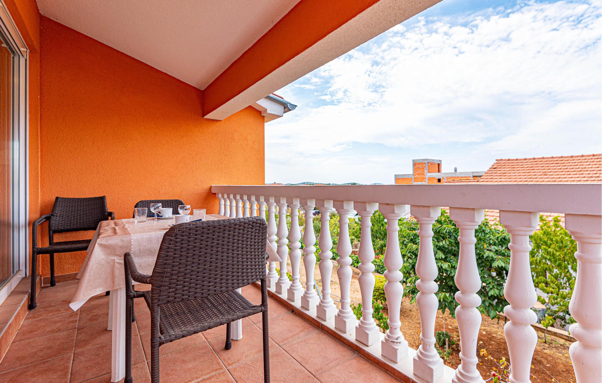 A balcony with a table and chairs, white balustrade, and a view of greenery and buildings.