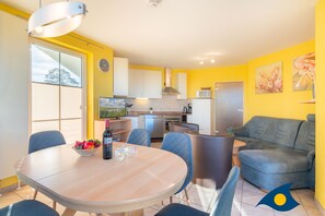 A modern kitchen with white cabinets, a dining table with chairs, and a sofa in a yellow-walled living area.