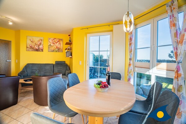 A bright yellow room with a round dining table, grey upholstered chairs, and a sofa.