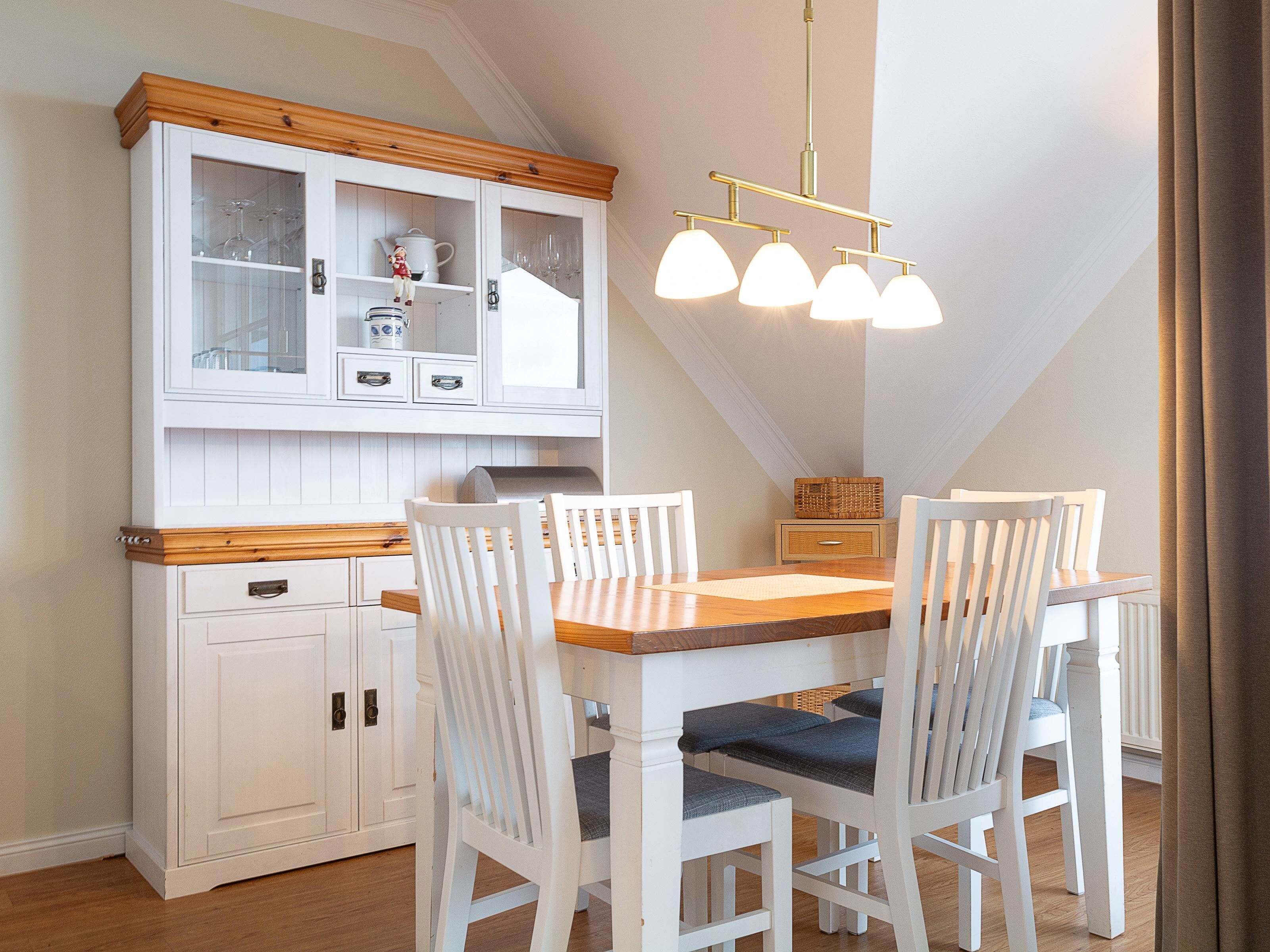 A dining area with a wooden table, white chairs, a white cabinet with glass doors, and a hanging light fixture.