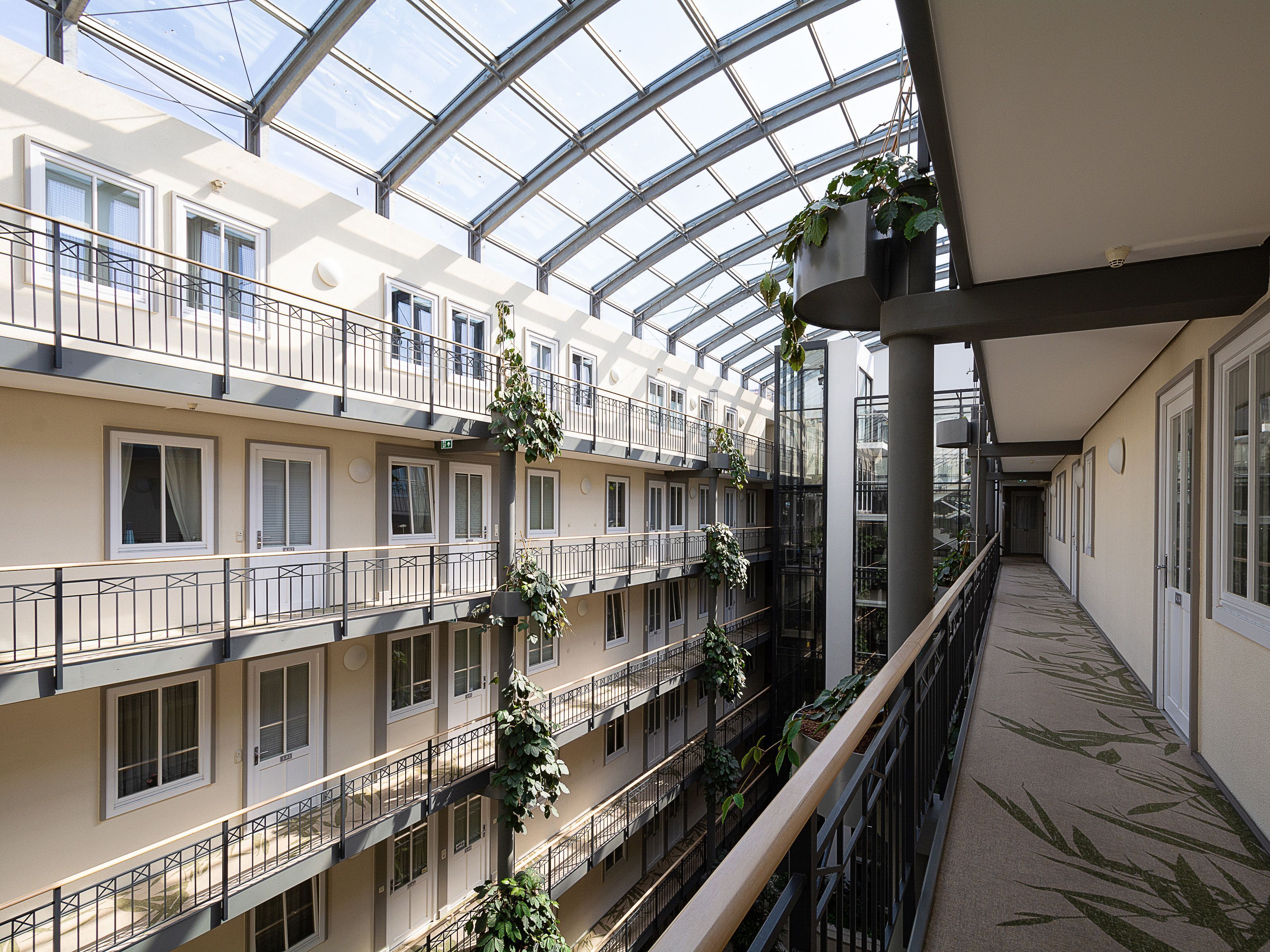 Een meerlaags atrium met balkons, grote ramen en hangplanten.