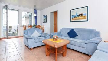 Ein Wohnzimmer mit zwei hellblauen Sofas, einem Holztisch und einem Gemälde von einem Leuchtturm.